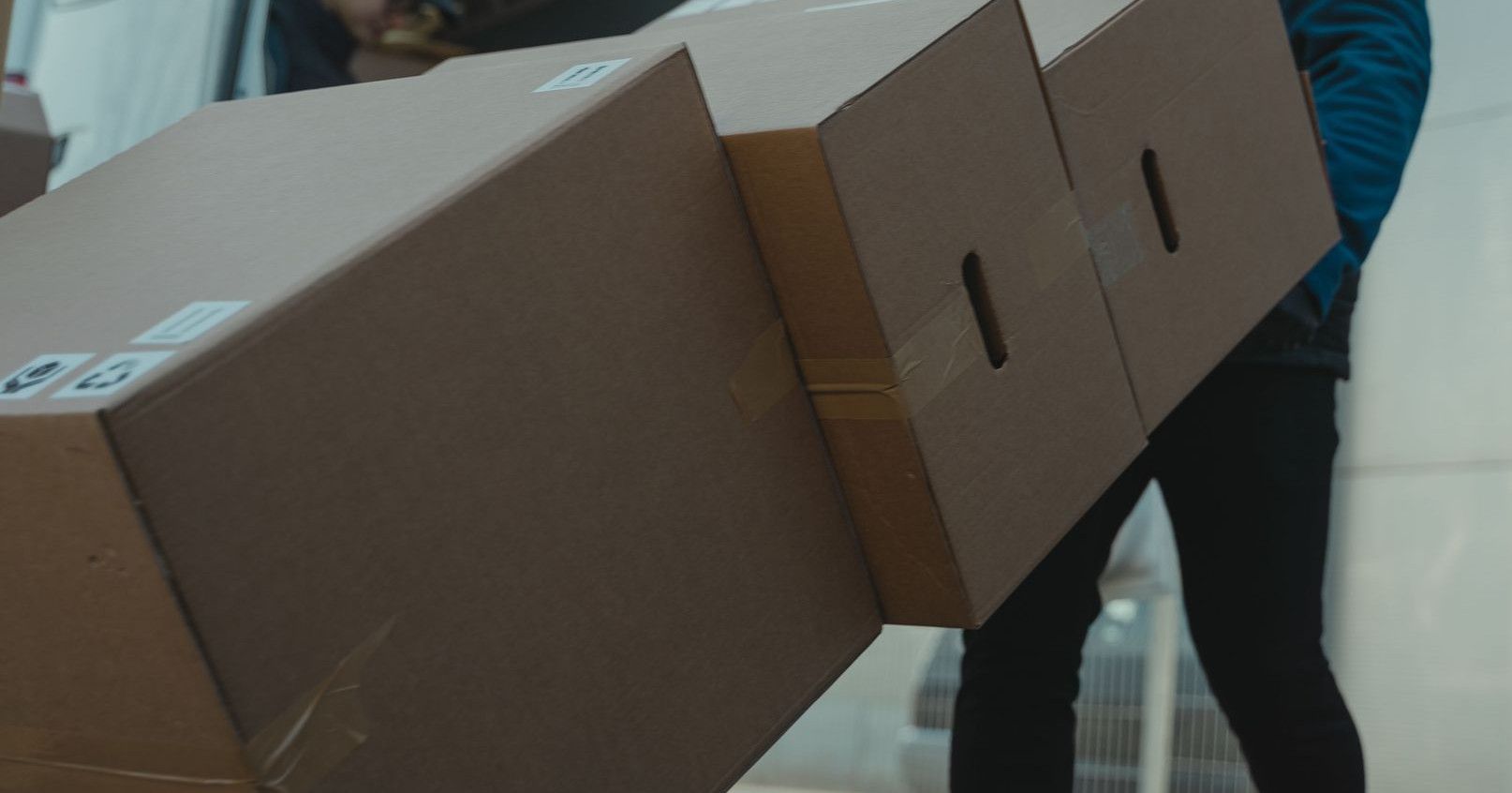 Delivery man carrying cardboard boxes from a van outside a modern building.