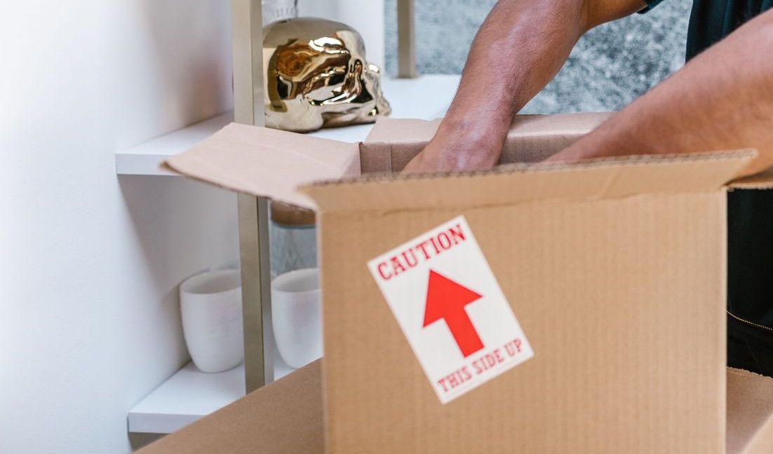 A professional mover packs a fragile item into a box in a stylish room.