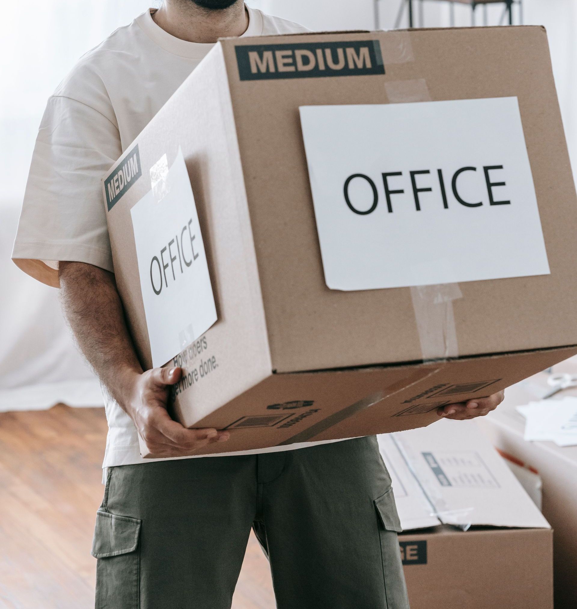 Man moving box labeled 'Office' indoors during relocation or packing.