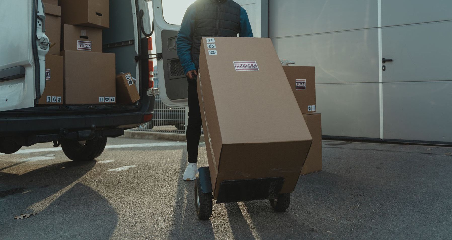 Delivery man with trolley unloading boxes from a van outside a warehouse.