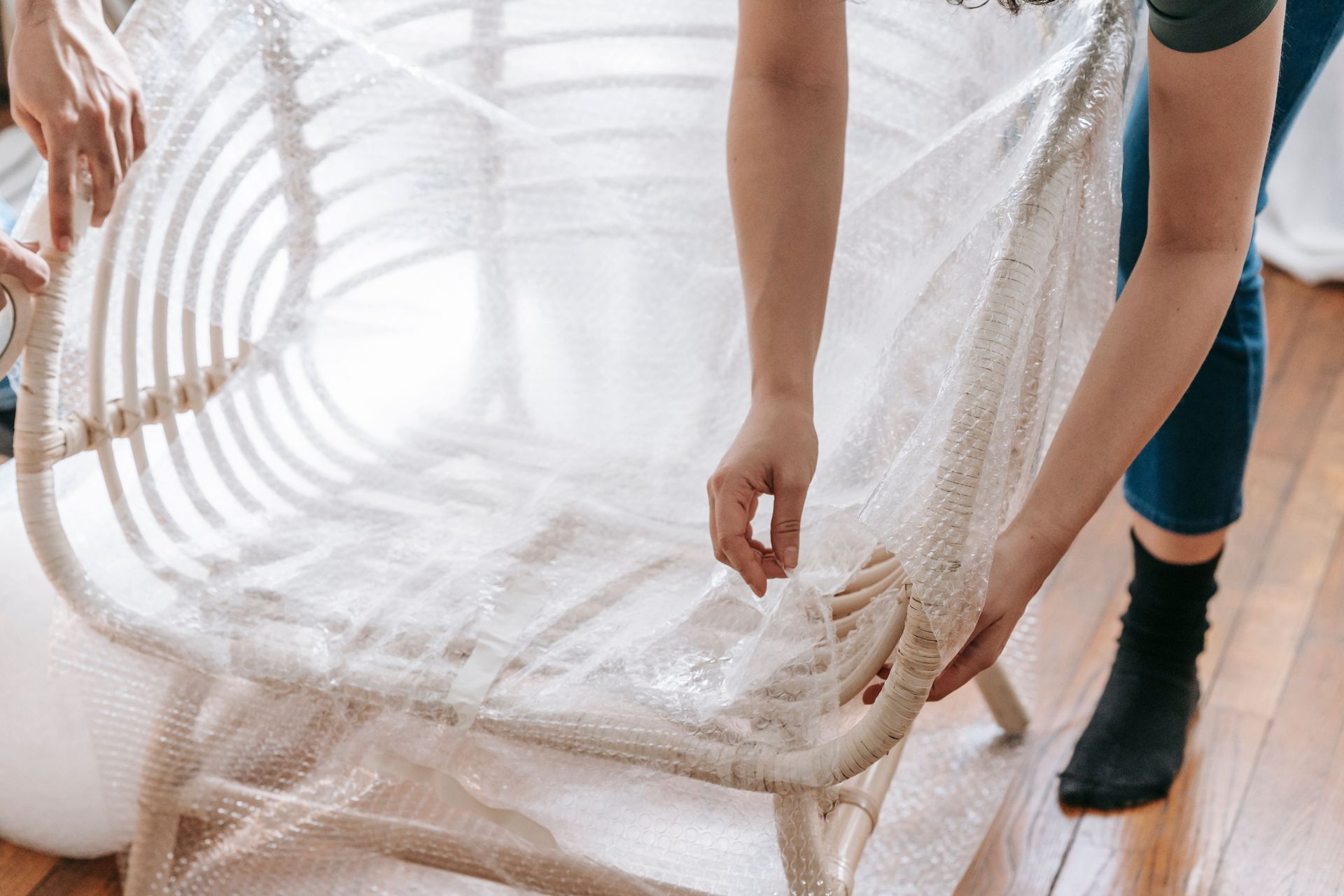 Close-up of a person wrapping a wooden chair in bubble wrap, preparing for moving or storage.