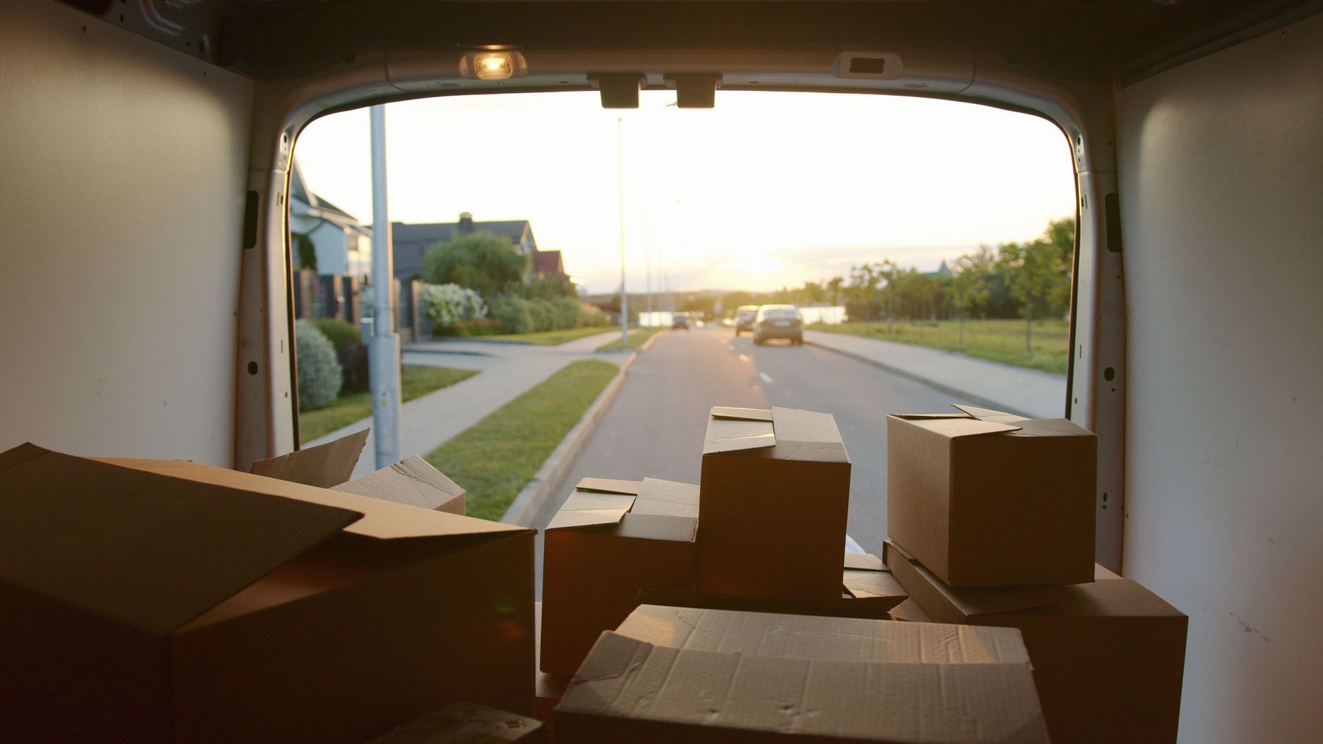 A scenic view from a delivery van loaded with cardboard boxes at sunset on a suburban street.